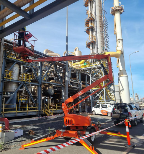 Technician on an elevated work platform installing equipment at an industrial site